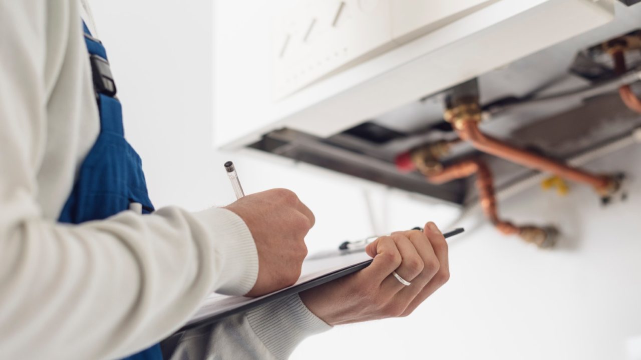 Professional plumber checking a boiler at home and writing on a clipboard
